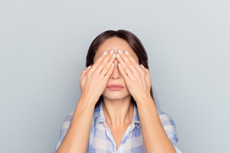 Close up portrait of tired woman after long working day on computer having eye problem, pressure, covering face, eyes with hands, afraid to look, standing over grey background