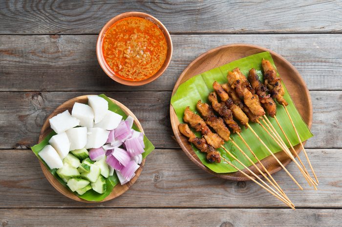 Overhead view Malaysian chicken sate with delicious peanut sauce, ketupat, onion and cucumber on wooden dining table, one of famous local dishes.