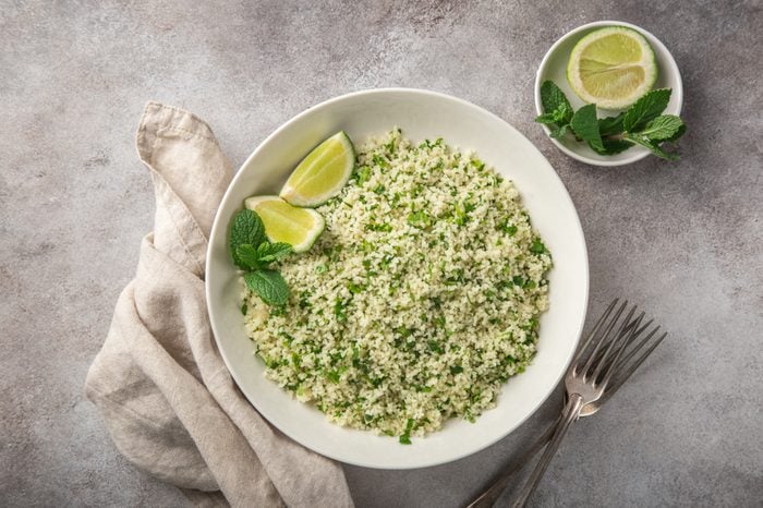 cooked couscous with lemon and herbs in white bowl, top view