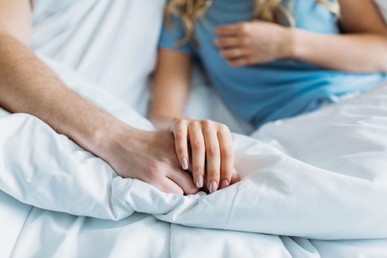 cropped image of couple holding hands in bed