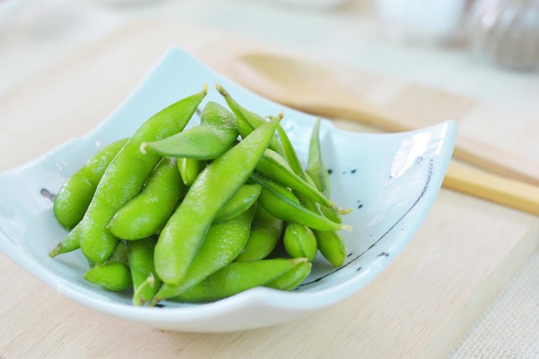 Clese-up edamame, or edamame bean in white square plate on wood bread board.