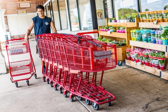 Happy Trader Joe's employee returning shopping carts to the store outside entrance with woman customer