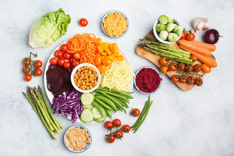 Vegan salad, top view of buddha bowl, colourful vegetables, carrot, courgette, cabbage, chickpeas, cucumber and tomatoes, on wooden board on white table, copy space, top view, selective focus