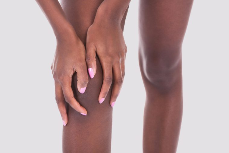 Midsection of African American woman suffering from knee pain against white background