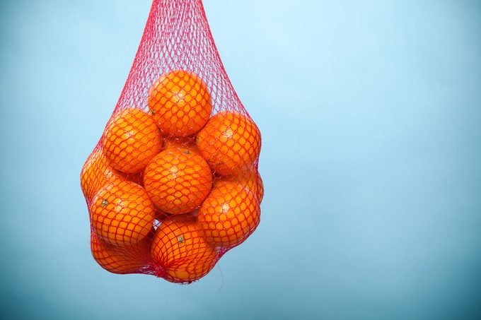 Mesh bag of fresh oranges healthy tropical fruits from supermarket on blue. Food retail.
