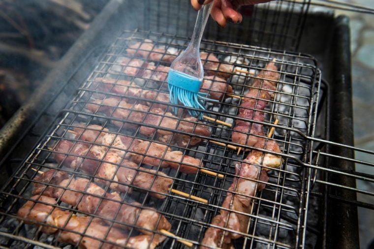 A woman puts olive oil on Souvlaki during barbecue.