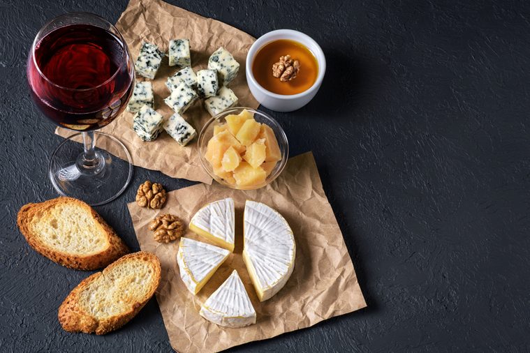 Camembert cheese, blue cheese, parmesan, toasts, honey, walnuts and glass of wine on a dark background. Flat Lay.