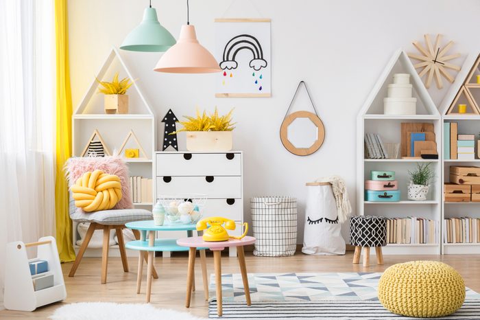 Yellow pouf near pink table with a phone in pastel kid's playroom interior with poster on white wall