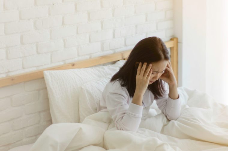 Asian women are headache severely.Lady wake up in the morning with migraine.Insomnia results in headaches when awakened.Young girl sitting on a stressed bed. In her bedroom.She was sick.Warm tone