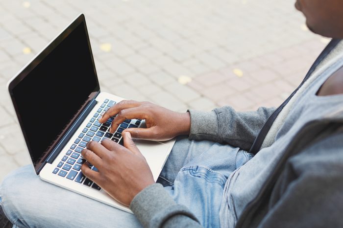 Мужские руки печатают на ноутбуке крупным планом.  Черный мужчина работает на открытом воздухе за компьютером с пустым экраном для копирования.  Технология, связь, образование и концепция удаленной работы.