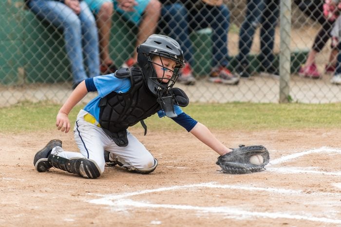 Agile little league baseball catcher lunging for a low pitch in the dirt in a cloud of chalk.