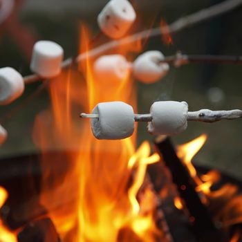 Multiple marshmallows extended over a camp fire to roast.