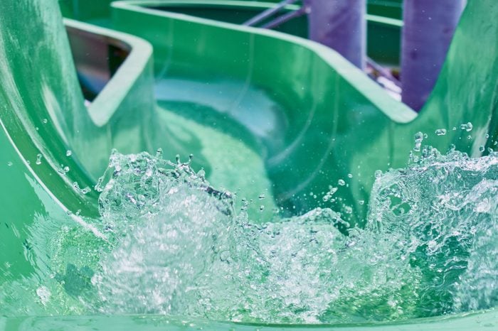 The stream of splashing water on green hill in water park for riding children