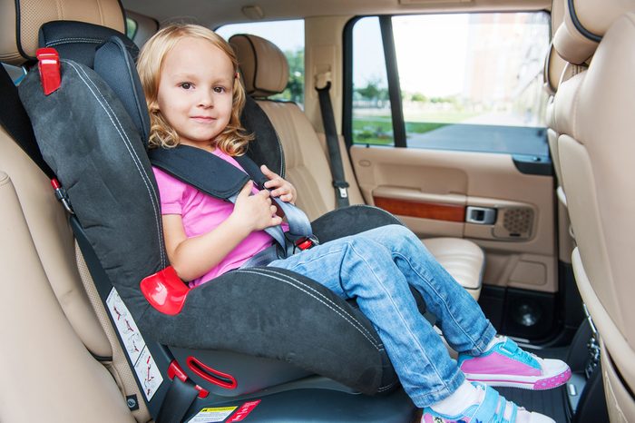 Small girl is sitting in child cat seat, looking at the camera