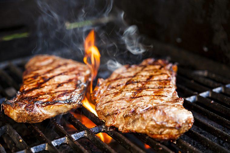 Beef steaks cooking in open flame on barbecue grill
