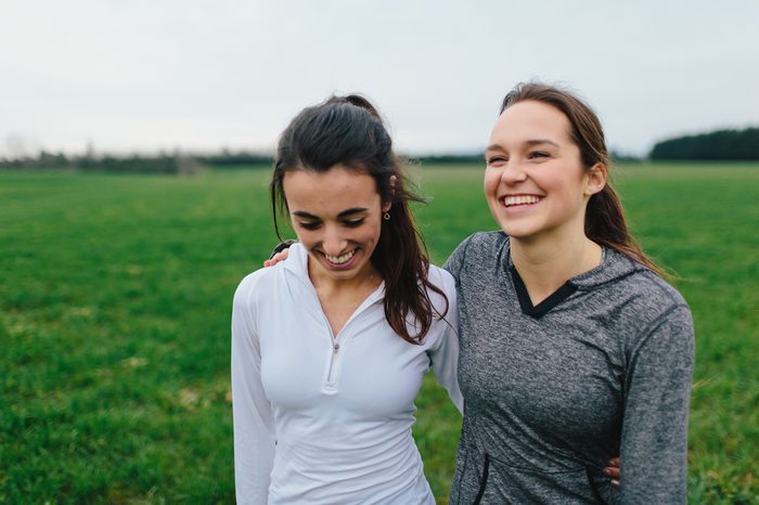 Young Adult Female Runners Arms Around each other smiling in country field
