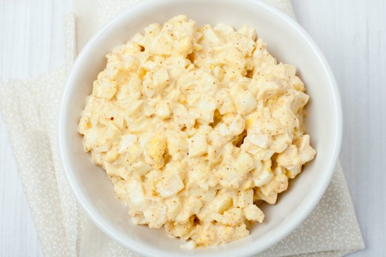 homemade egg salad in white bowl on white background, top view