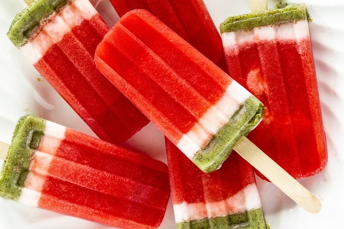 Close up of frozen fresh fruit watermelon and kiwi popsicles sitting on white plate