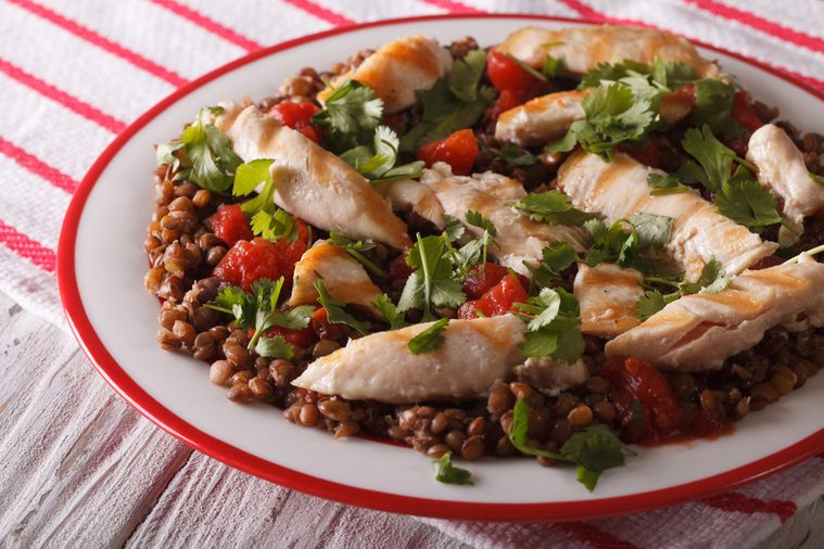 breakfast of brown lentils with grilled chicken and herbs close up on a plate. horizontal