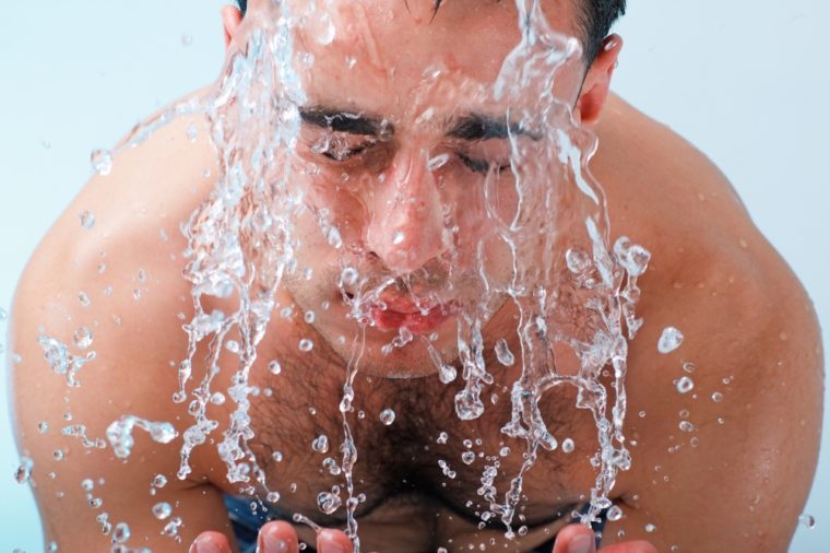 Young man washing face on a blue background.