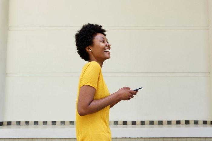Side portrait of cheerful young african woman walking with a mobile phone