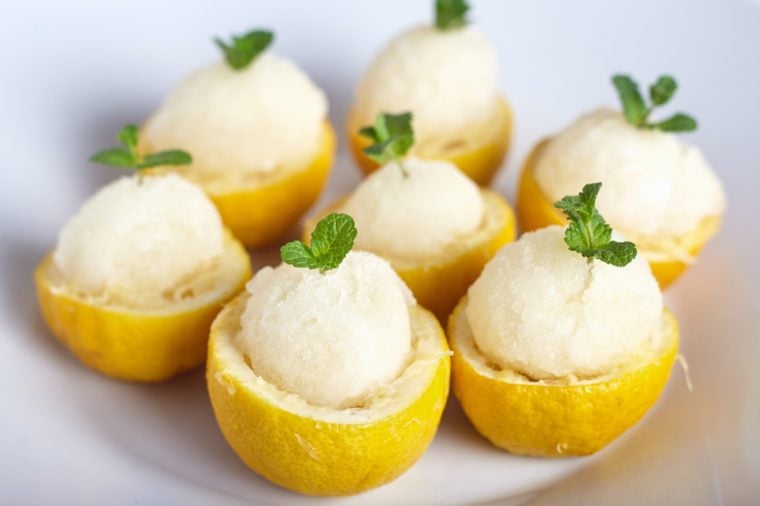 Lemon sorbet or ice cream inside fresh lemons decorated with mint leaves on big white plate