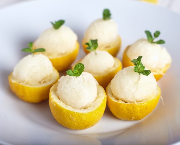 Lemon sorbet or ice cream inside fresh lemons decorated with mint leaves on big white plate