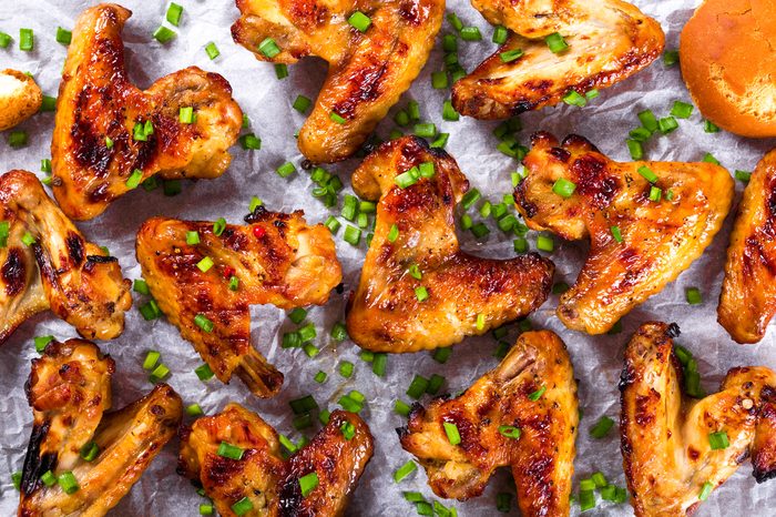 tasty roasted Ginger and honey chicken wings on a parchment paper with spices, toasted bread and spring green onion, top view, close-up