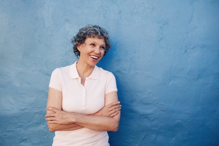Portrait of smiling senior woman standing with her arms crossed and looking away at copy space against blue background. Caucasian middle aged female looking happily at copy space.