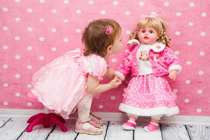 little girl on a pink background playing with a doll