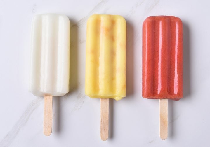 top view of three different ice pops on a marble counter top. Red, yellow and white fruit flavored frozen treats.