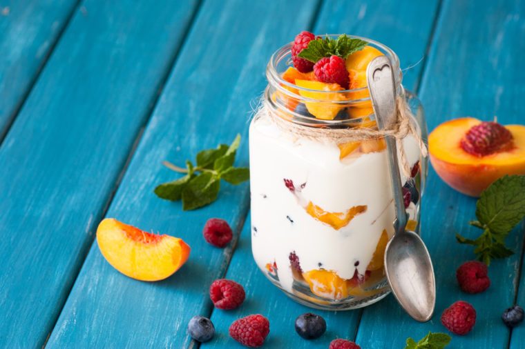 Fruit and berries dessert in a mason jar on blue table. Fruit salad with yogurt or sour cream.