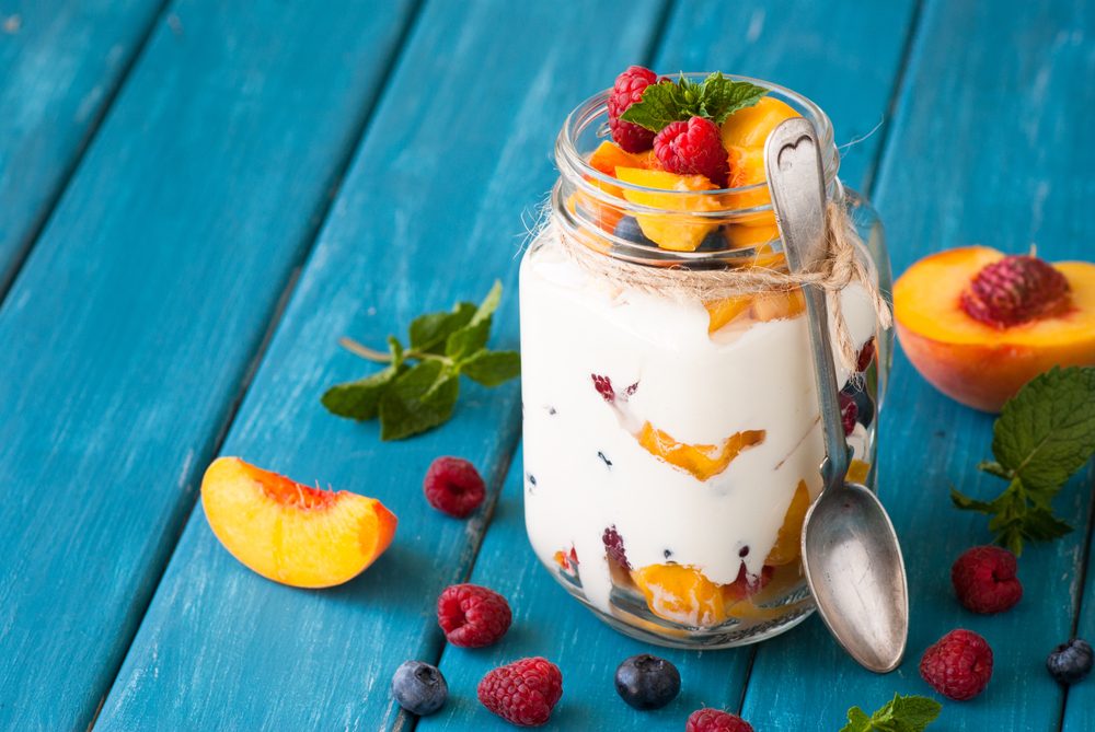 Fruit and berries dessert in a mason jar on blue table. Fruit salad with yogurt or sour cream.