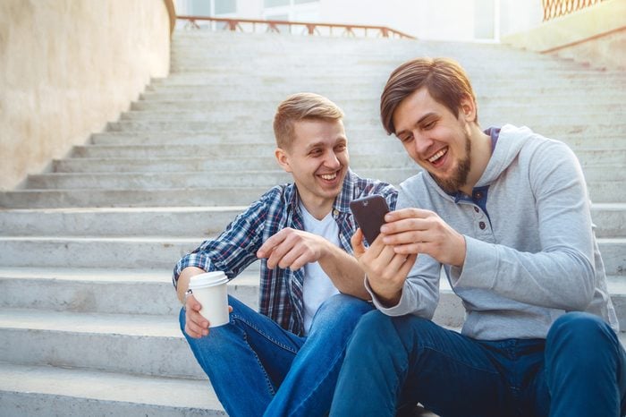 Two young men sitting on the steps and laughing, looking at the phone