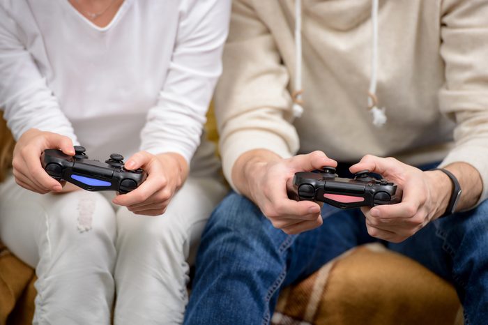 Close up photo of young friends playing video games in living room. Focus on hands and controllers