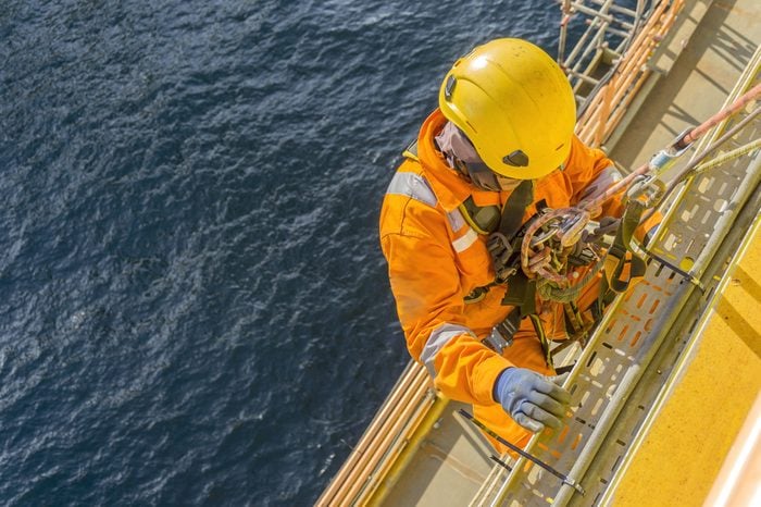 Man working overboard. Abseiler complete with personal protective equipment (PPE) climbing and hanging at the edge of oil and gas rig platform in the middle of sea.