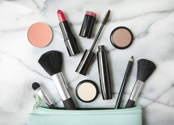 Overhead view of make up products spilling out of a pastel blue cosmetics bag, on a white marble counter top background