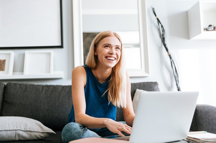 Cheerful cute young woman using laptop and laughing at home