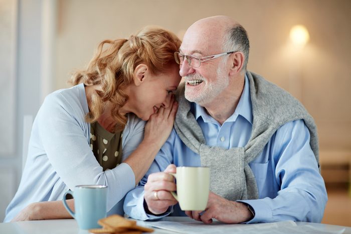 Portrait of smiling senior couple sitting close together cuddling caringly and laughingat kitchen table with tea cups and homemade cookies