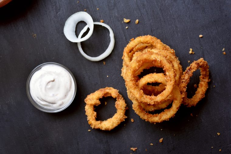 Crunchy fried onion rings and white sauce on dark background, top view