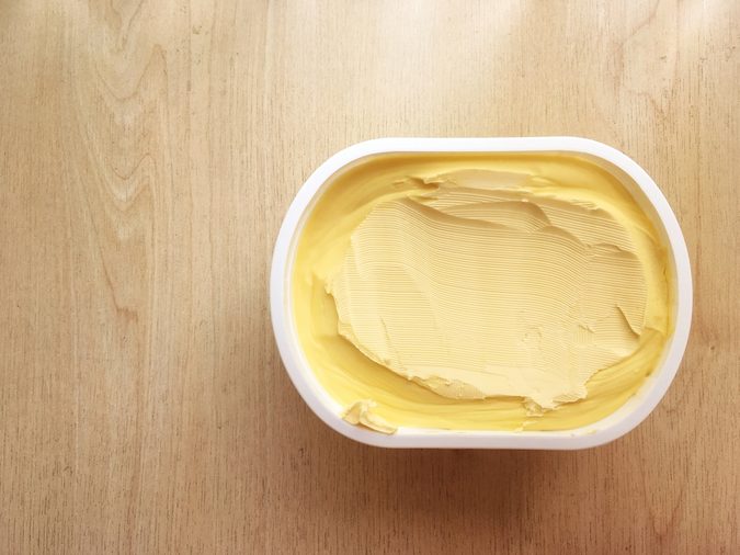 Top view looking down onto a tub or pot of butter or golden yellow spread on wooden background with natural window light.