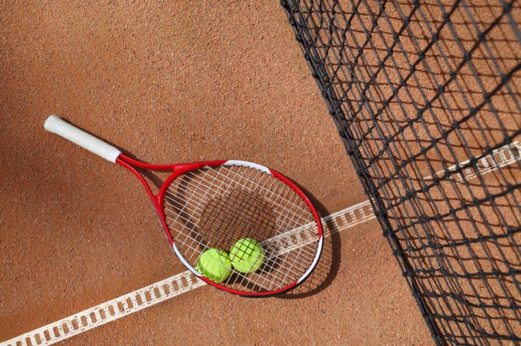 Tennis racket and two balls near net on court at sunny summer day