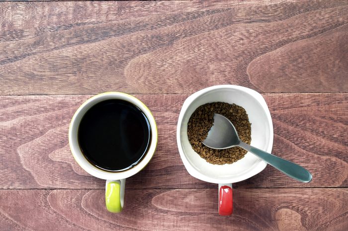 black coffee and instant coffee with silver spoon in coffee cup on brown wooden table floor, close up top view two cups