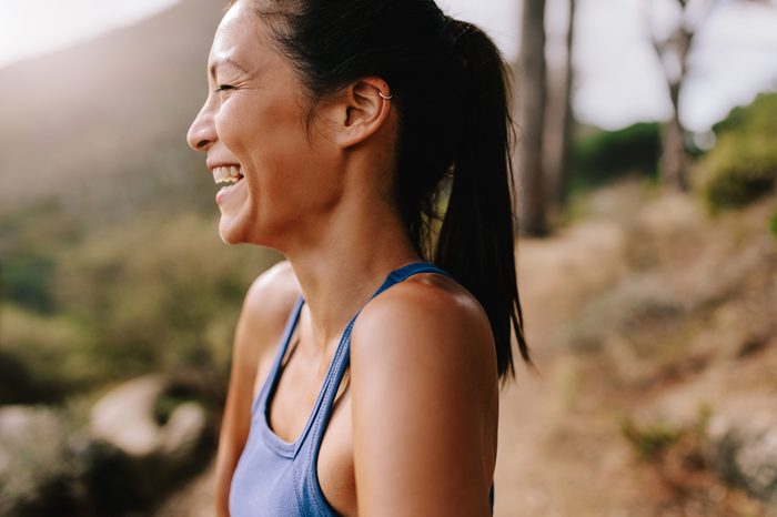 Side view shot of fit young woman standing outdoors, looking away and laughing. Happy female runner in sportswear in morning.