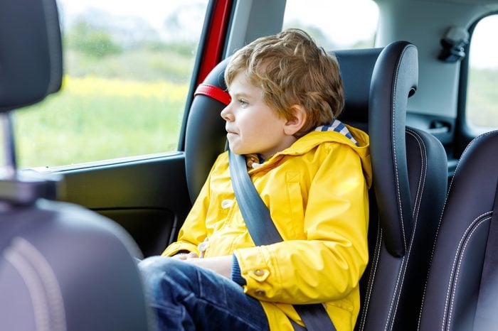 Adorable cute preschool kid boy sitting in car in yellow rain coat. Little school child in safety car seat with belt enjoying trip and journey. Safe travel with kids and traffic laws concept.