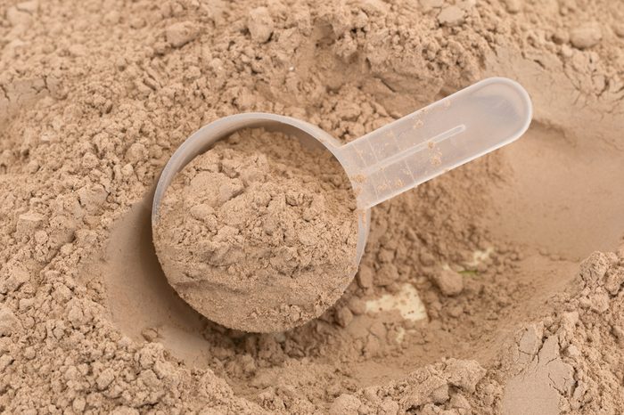 Close of ground chocolate flavored plant protein with a plastic measuring scoop.