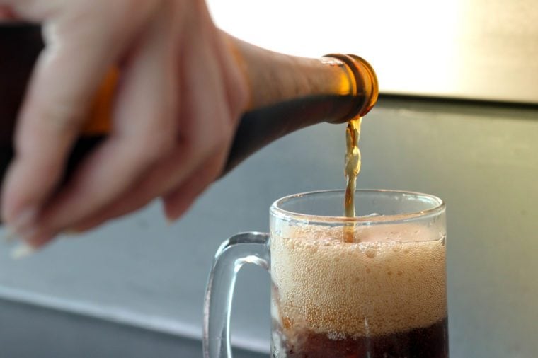hand hold and pour root beer to glass , ice cola