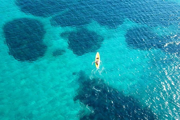 Aerial drone bird's eye view of kayak cruising in tropical rocky seascape with turquoise and sapphire clear waters