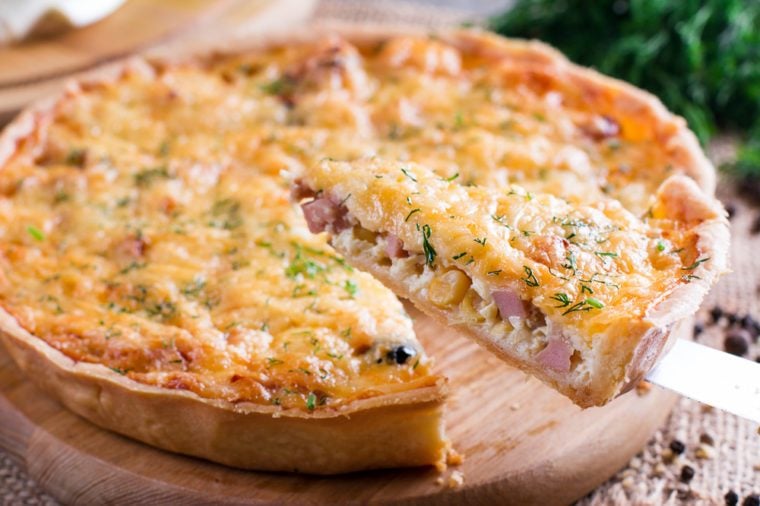 A piece of onion cheese quiche or pie sprinkled with parsley on wooden table. Horizontal