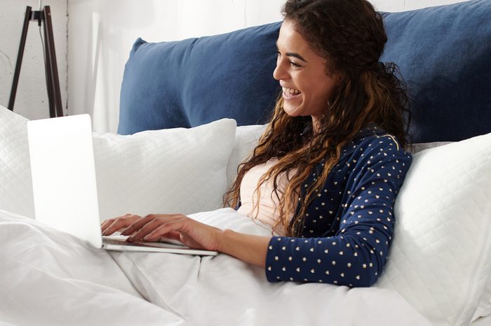 Happy casual beautiful woman with spread hands working on a laptop laying on the bed in the bedroom